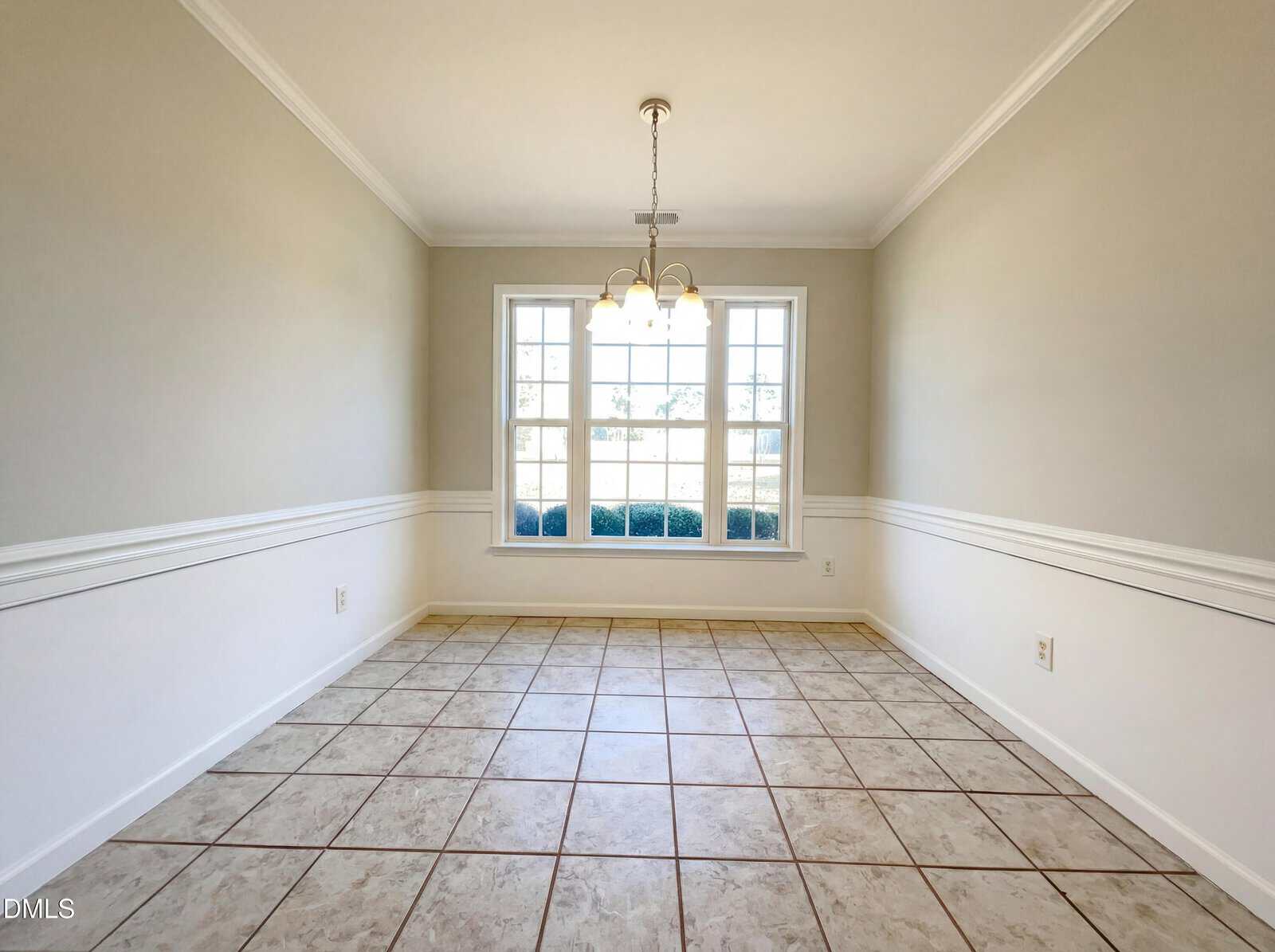 Empty dining room with beige tiled floor, light gray walls with white trim, a large window letting in natural light, and a ceiling light fixture hanging in the center of the room.