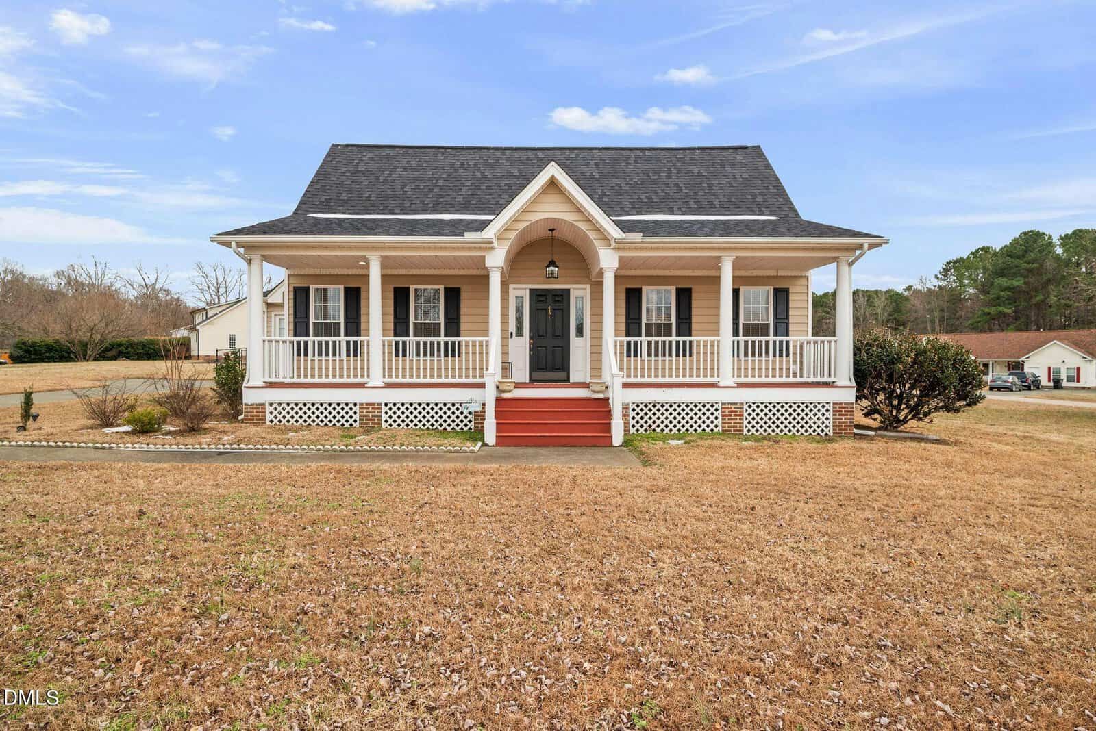 A single-story beige house with a black roof, white trim, and a covered front porch with railings and columns sits at 30 Woodcrest Drive in Youngsville. The front yard has dry grass, and there are a few houses and trees in the background under a blue sky.
