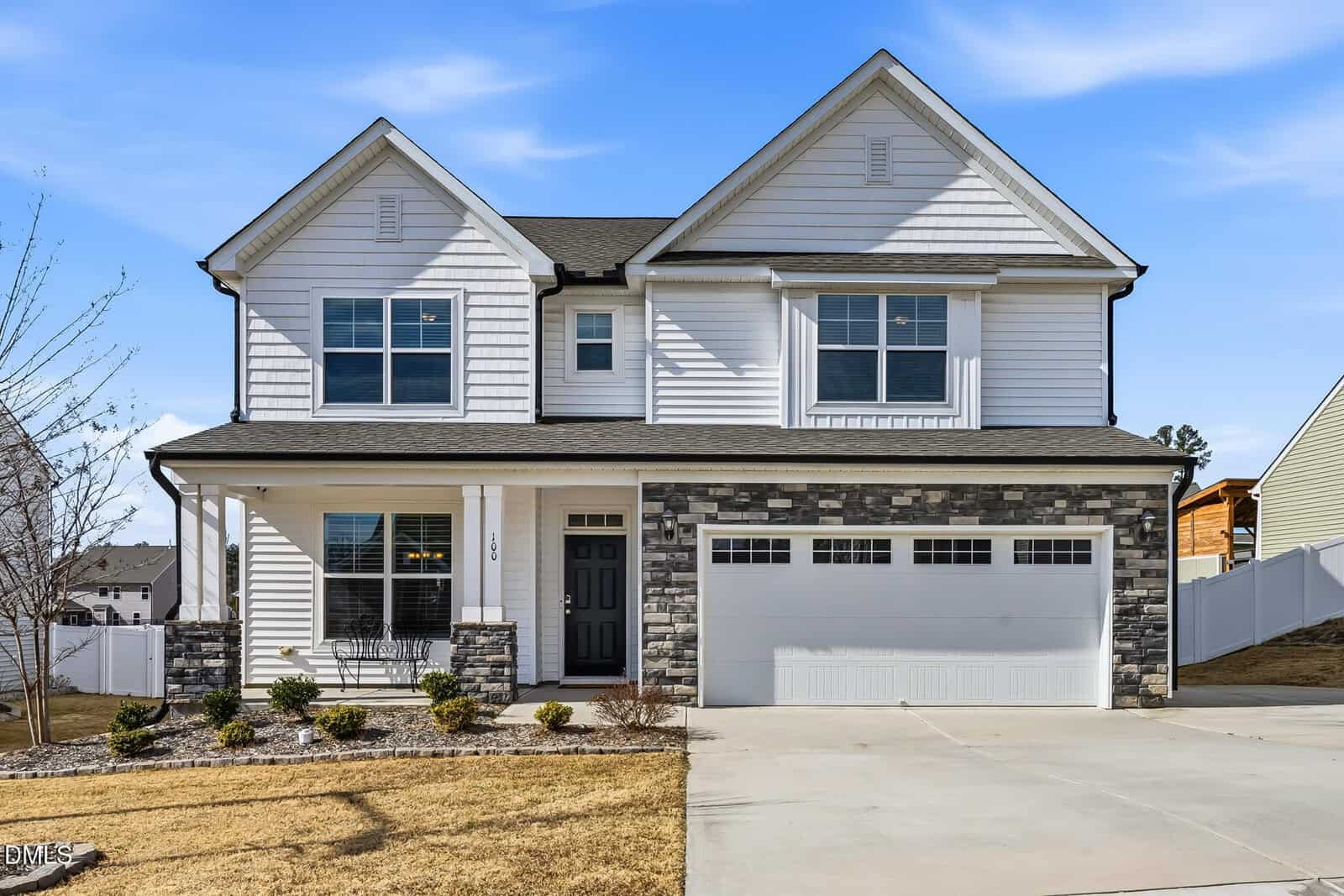 Two-story suburban house with white siding, black roof, and stone accents located at 100 Mallory Oak Drive in Franklinton. Features a covered front porch, black front door, two-car garage, and a driveway. The yard has minimal landscaping with a few small bushes.