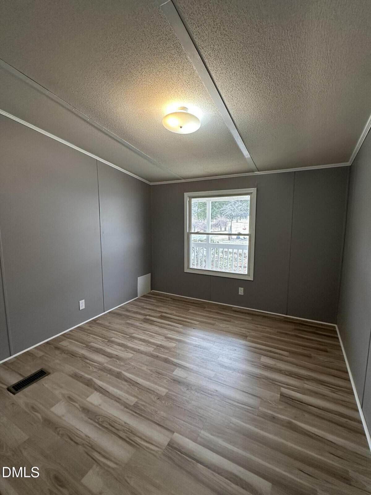 Empty room with gray walls, wood-style flooring, a ceiling light, white trim, and a window letting in natural light.