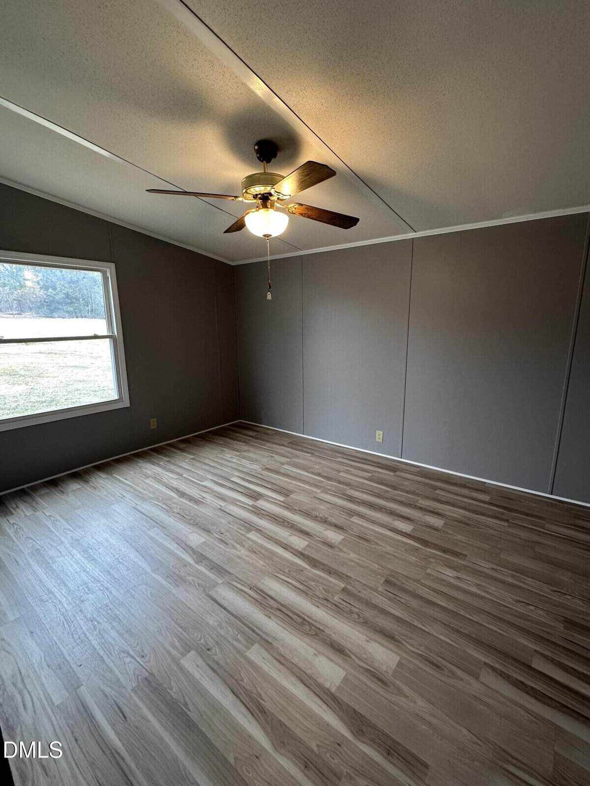 Empty room with wood-style flooring, gray walls, a single window letting in natural light, and a ceiling fan with a light fixture.