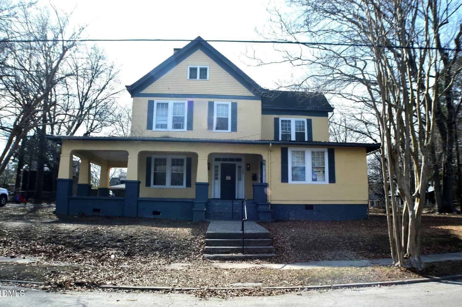 Two-story yellow and blue house with a covered front porch, multiple windows, and a central entryway located at 169 Burwell Avenue in Henderson. The yard is mostly bare with some leaves, trees without leaves, and a sidewalk leading to the steps.