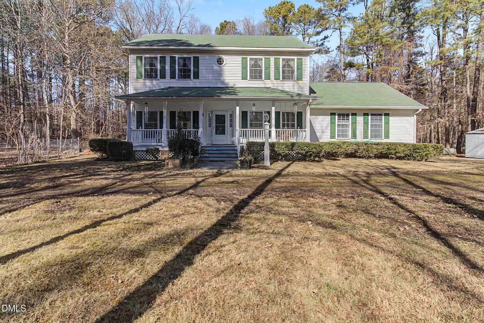 Two-story house with green shutters and a green roof, white siding, a front porch with steps, and several windows. Located at 4311 Old North Carolina 75 in Oxford, the property features a large brown lawn bordered by bushes and is surrounded by tall trees with no leaves.