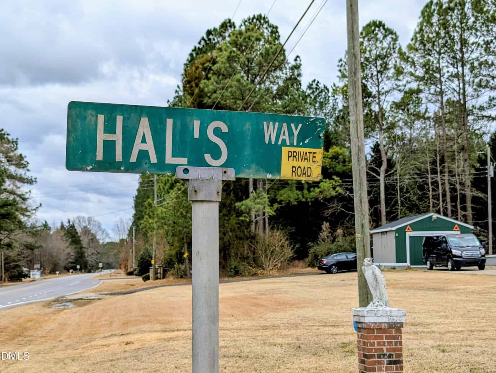 A green street sign reads “HAL’S WAY” with a smaller yellow sign below stating “PRIVATE ROAD.” The signs are mounted on a post near a rural road lined with trees and a green building in the background, marking the entrance to 26 Hals Way in Franklinton.