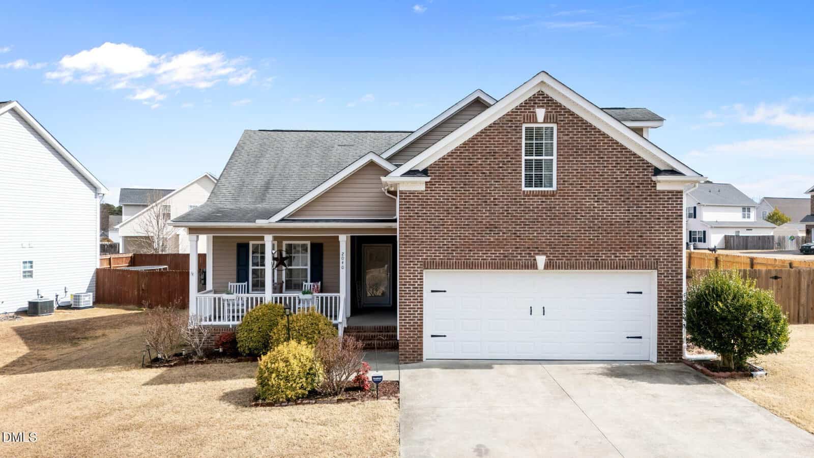 A single-story brick and siding house at 2040 Applewood Drive in Creedmoor features a welcoming front porch with white railing and a spacious two-car garage. The driveway is bordered by small shrubs that line the front yard, while the sky above is mostly clear with some clouds.
