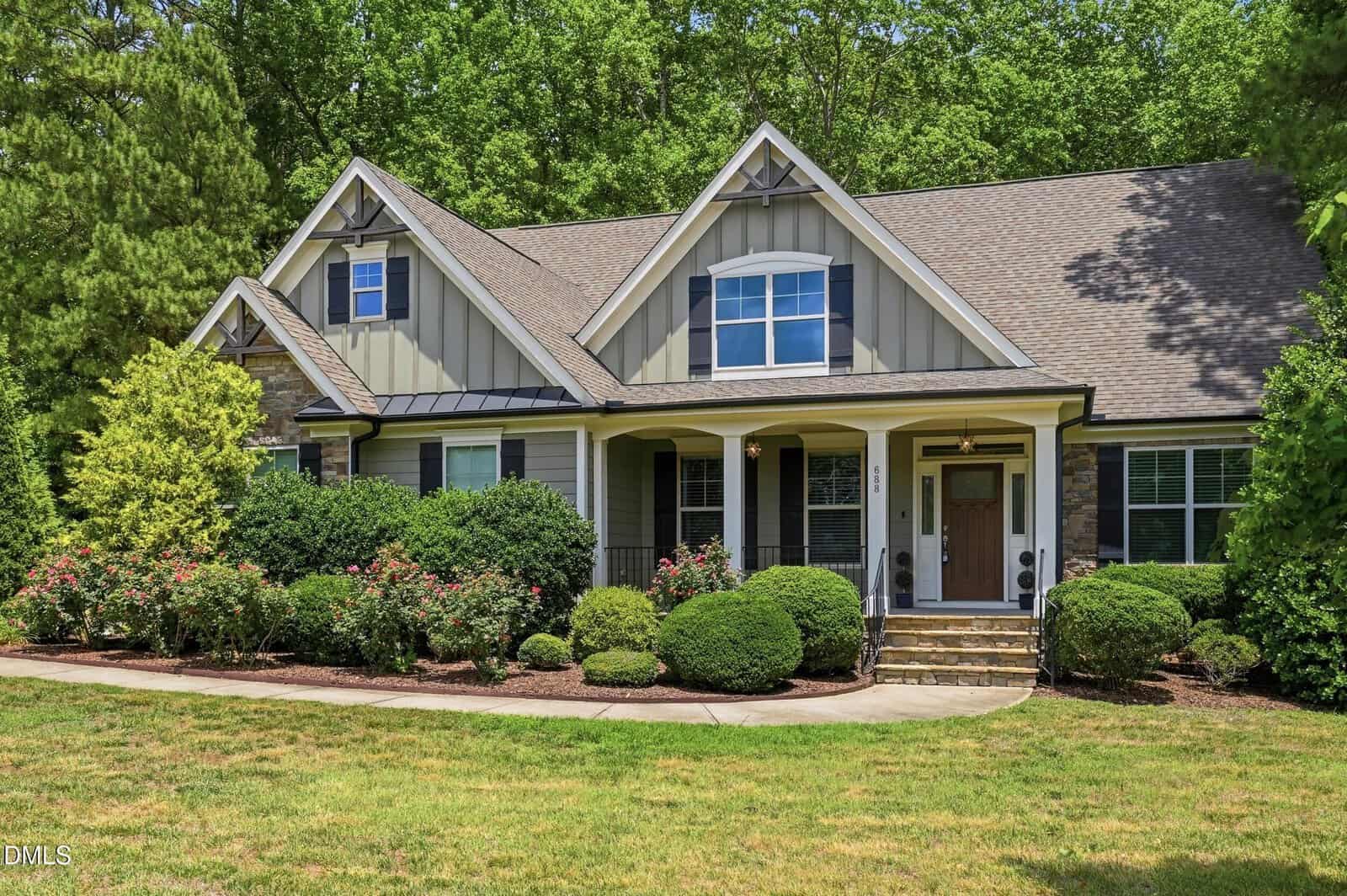 This single-story house at 688 Willard Drive in Creedmoor features gray siding, white trim, a gabled roof, and a covered front porch. The landscaped yard includes bushes, shrubs, a well-kept lawn, and tall trees in the background.