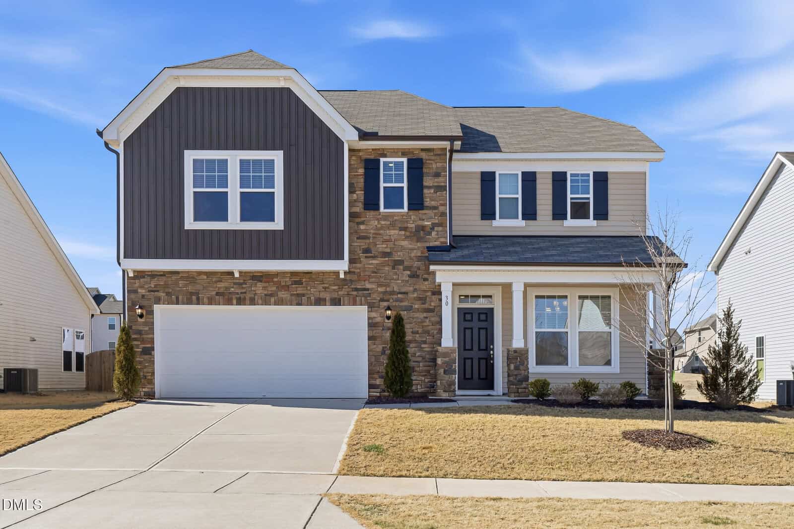 Two-story suburban house at 30 Junius Birch Trail, Franklinton, featuring a mixed stone and siding exterior, attached two-car garage, black front door, and small front yard with minimal landscaping. The driveway leads to the garage, and the sky is clear.