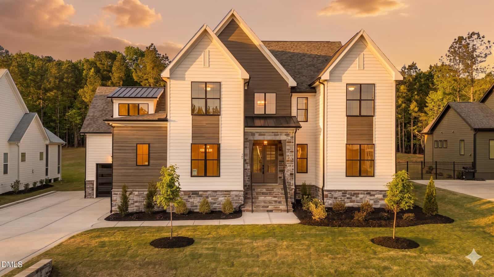 Modern two-story house at 125 Cherry Bark Drive, Youngsville, with white and brown siding, stone accents, large windows, and a front porch. Neatly landscaped yard features young trees and driveways on either side.