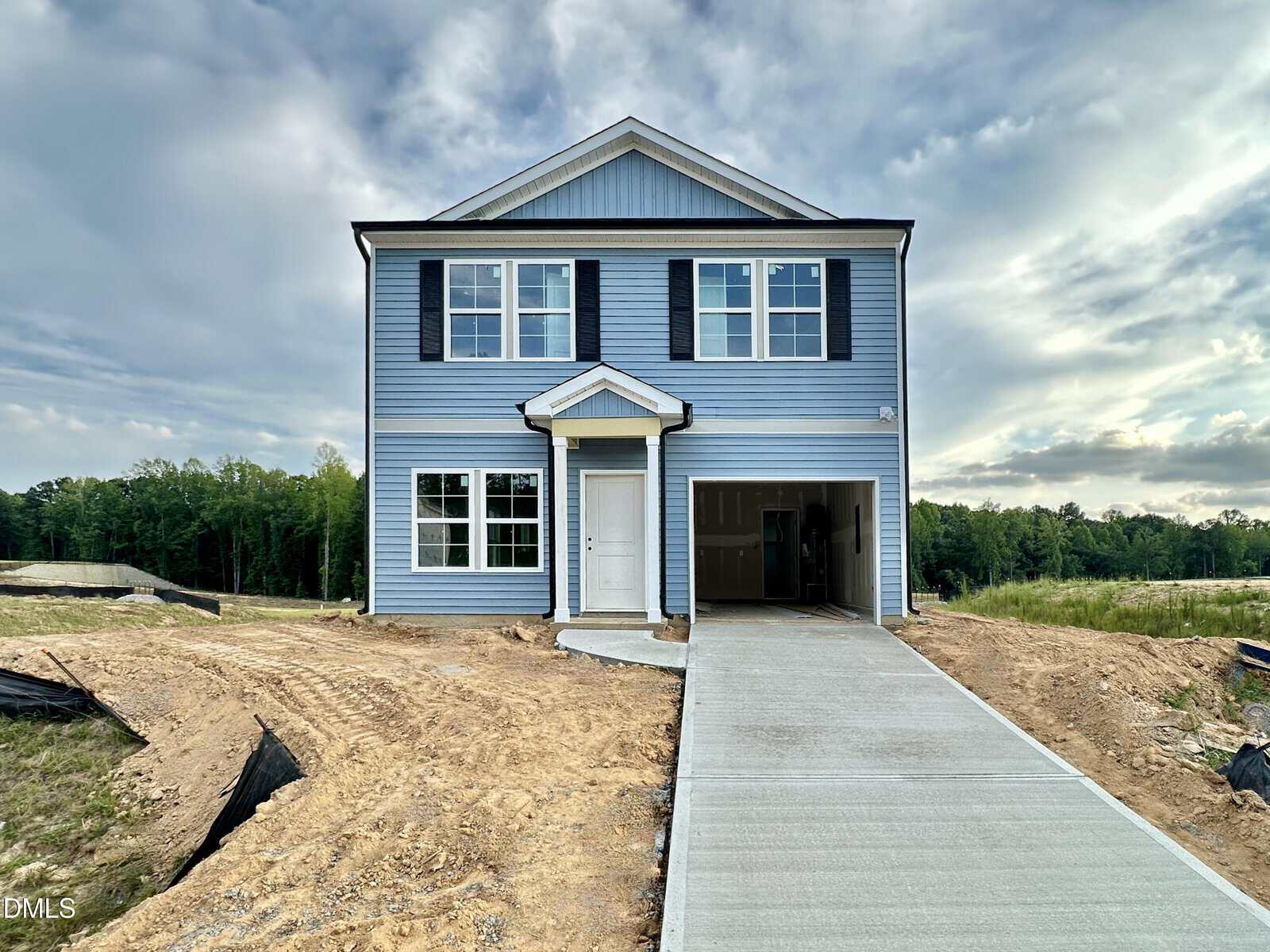 A newly constructed two-story blue house with white trim, a covered entryway, and an attached garage sits on a dirt lot with a fresh concrete driveway at 265 Buckthorn Drive in Youngsville, surrounded by grass and trees under a partly cloudy sky.
