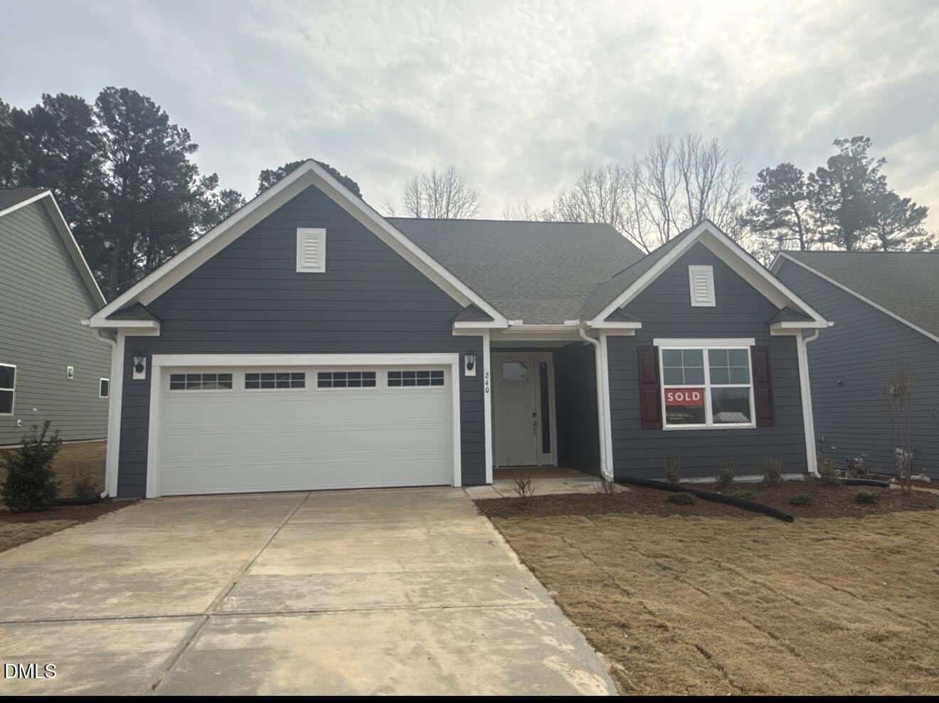 A single-story dark gray house with white trim, a double garage door, and a “Sold” sign on the front window sits on a concrete driveway with a newly landscaped yard and trees in the background at 240 Sawtooth Oak Lane in Youngsville.