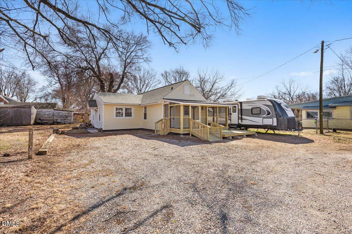 Single-story house with light-colored siding, a covered wooden porch with railings and a ramp, gravel driveway, leafless trees, and a parked travel trailer in the yard. Set on 248 Orville Street in Henderson, the property offers clear views of the sky and neighboring buildings.