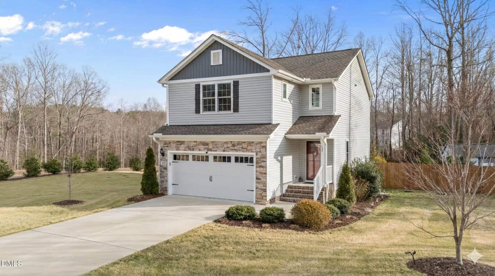 Two-story house with gray siding, stone accents, and a double garage. Located at 150 Teal Drive in Youngsville, the home features a front porch, driveway, and landscaped lawn, surrounded by trees and open grass under a blue sky.