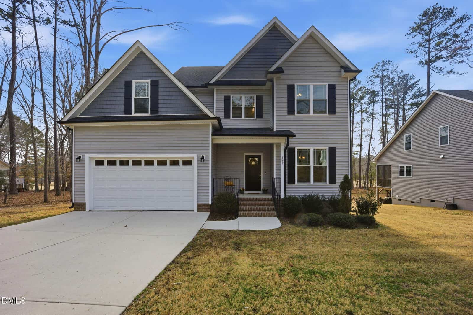 Two-story suburban house at 167 Black Cloud Drive in Louisburg, featuring gray siding, black shutters, and a two-car garage. A concrete driveway and front steps lead to a covered entrance. The lawn is neatly trimmed, and trees surround the property.