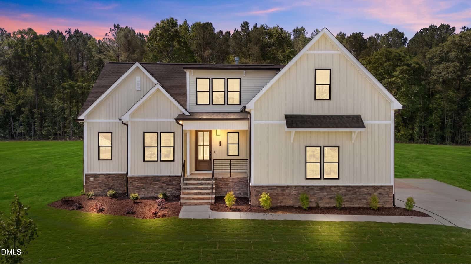Modern two-story house at 40 Stream View Way, Zebulon, with white siding, large windows, and stone accents, warmly lit at dusk. Features a front porch with steps, a neatly landscaped yard, and trees in the background.