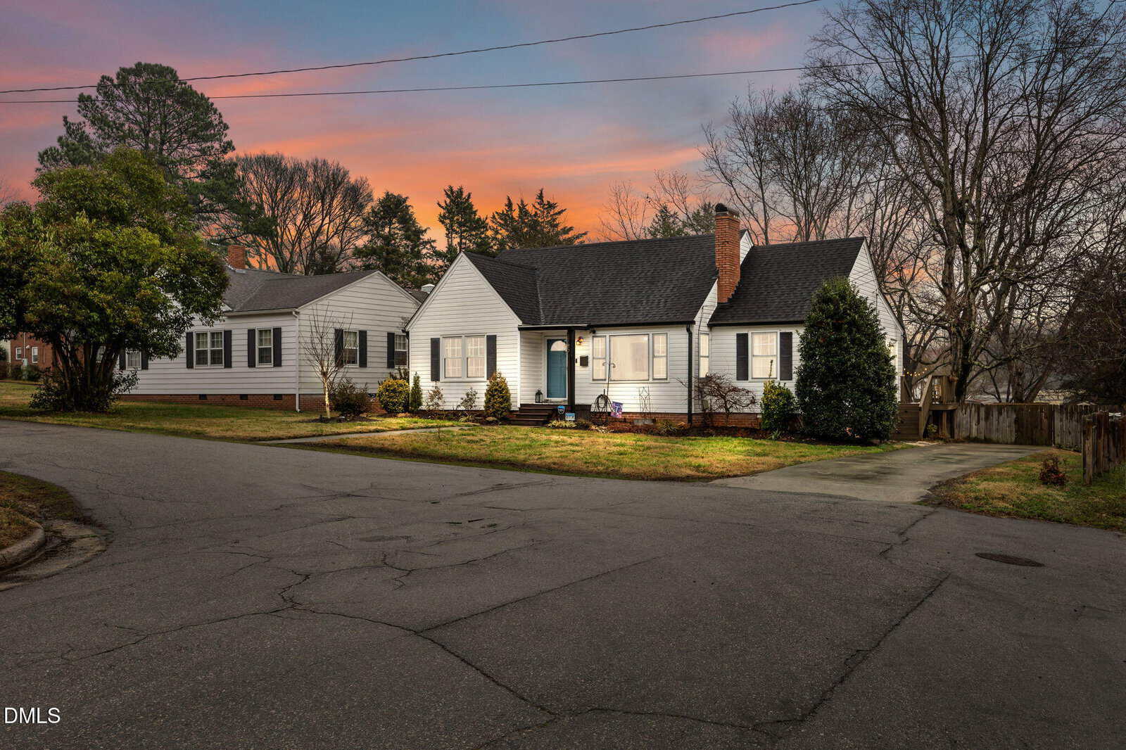 Single-story white house with dark roof, front porch, and brick chimney on a corner lot at 109 Grace Street in Oxford. Leafless trees and trimmed bushes surround the home. The driveway and street are visible. Sky shows a sunset with orange and blue tones.
