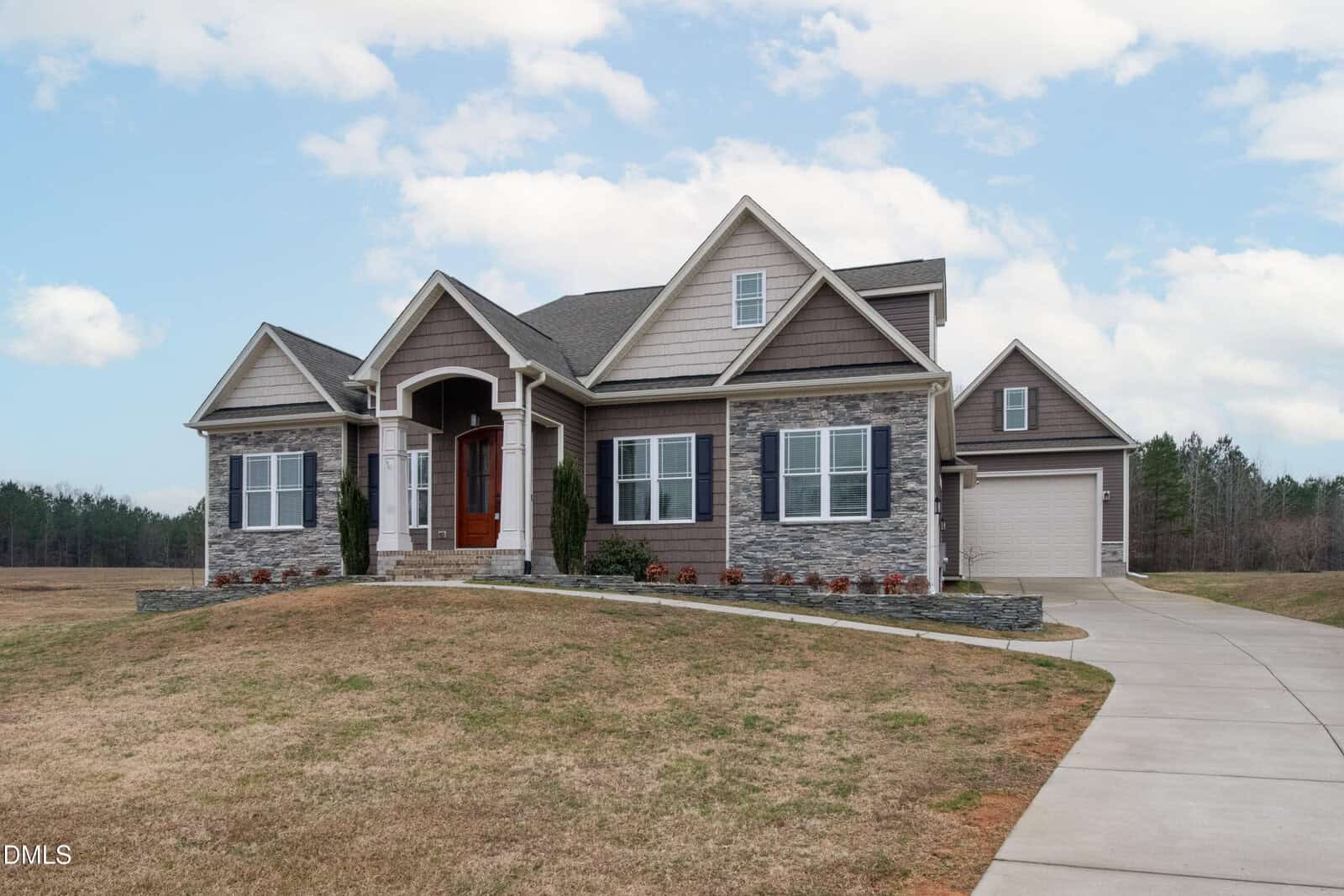 A modern suburban house with gray siding, stone accents, and a covered entryway located at 88 Stonewood Loop Lane in Henderson. There is a large attached garage and a curved driveway, surrounded by a grassy lawn and open landscape.