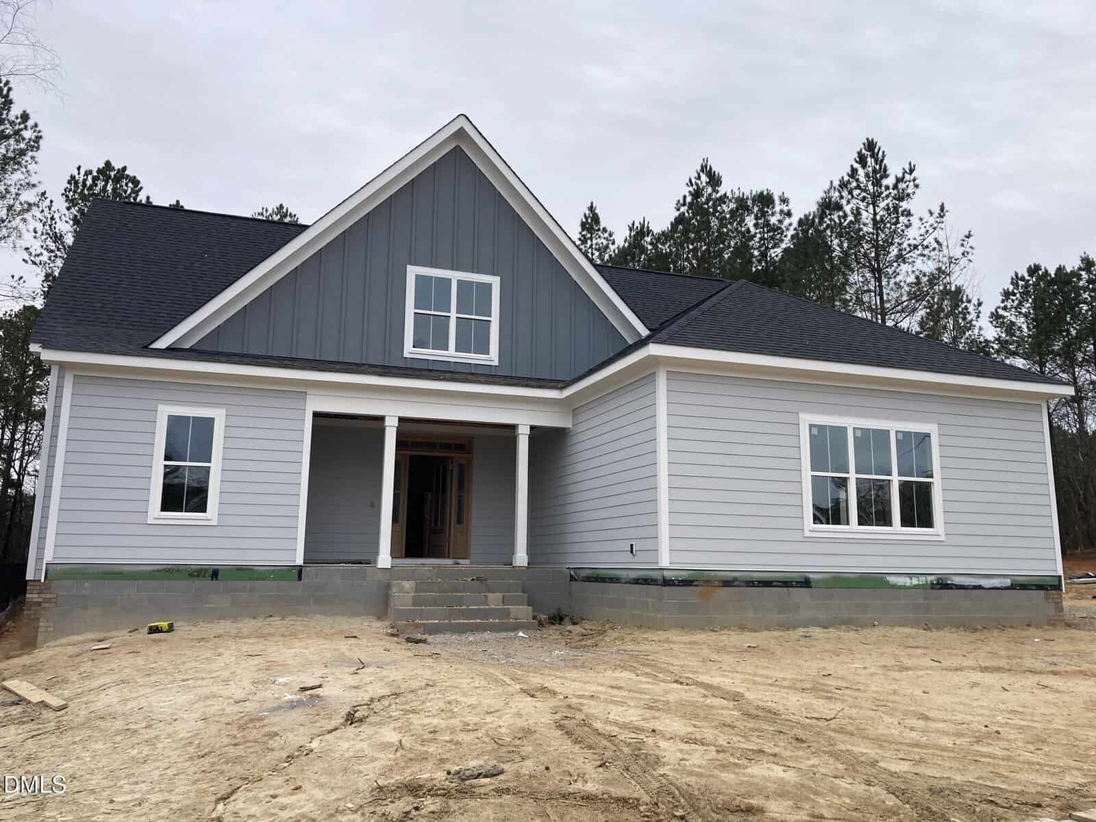 A newly constructed, single-story house with gray siding, white trim, a covered front porch with columns, and a black shingle roof sits at 1216 Red Cedar Court Lot 37 in Youngsville. The yard appears unfinished with bare soil in front of the home, while pines are visible in the background.
