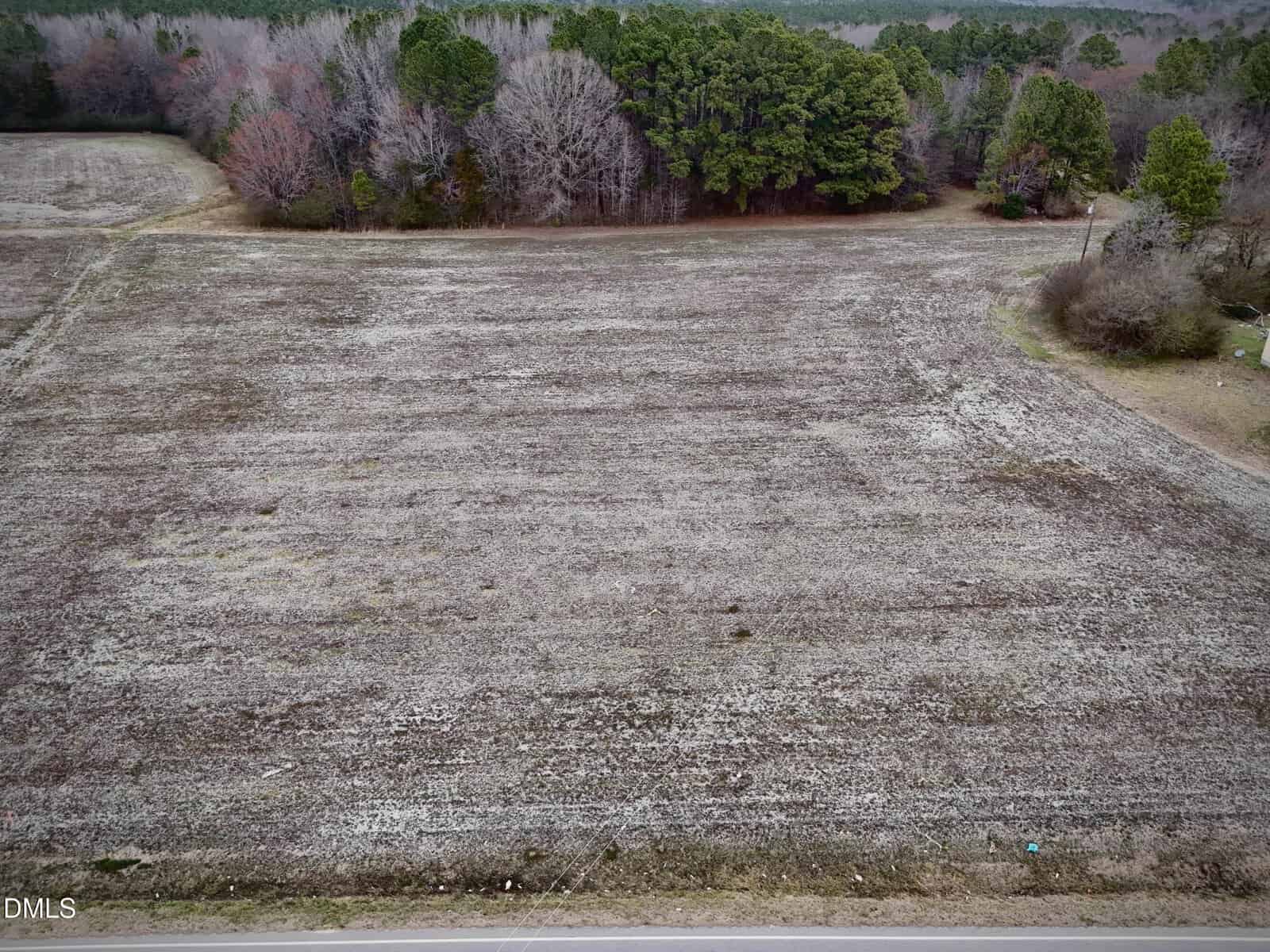 A flat, empty field with sparse grass borders a road in the foreground on Lot 5 W River Road, Franklinton. Leafless and evergreen trees line the back and right edges of the field under an overcast sky.