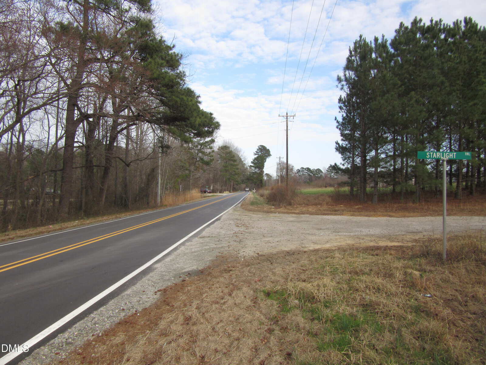 A two-lane road runs alongside trees on the left, with a gravel side road intersecting on the right near Lot 1 Johnson Town Road in Zebulon. A green street sign reads “Starlight.” Power lines run parallel to the road under a partly cloudy sky.