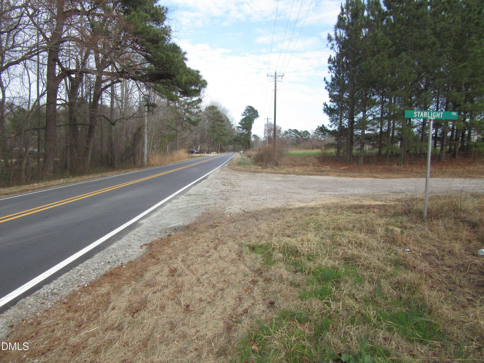 A paved two-lane road runs alongside a grassy roadside and trees. A gravel side road intersects, and a green street sign reads “Starlight.” Power lines and a cloudy sky are visible in the background.
