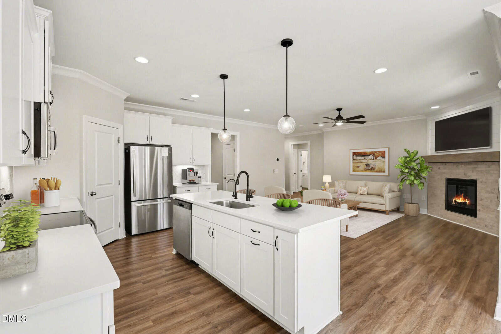 Modern open-concept kitchen and living room at 141 Taopi Drive, Louisburg, with white cabinetry, stainless steel appliances, pendant lighting, fireplace, wood flooring, and neutral walls. Sofa, artwork, and indoor plants add cozy decor.