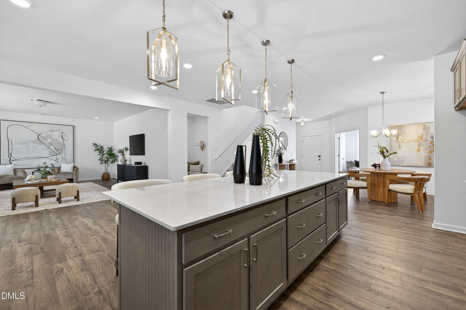 Modern open-concept kitchen and living space with wood floors, a large island with pendant lights, and dining area. Neutral colors and minimalist decor create a bright, airy atmosphere.