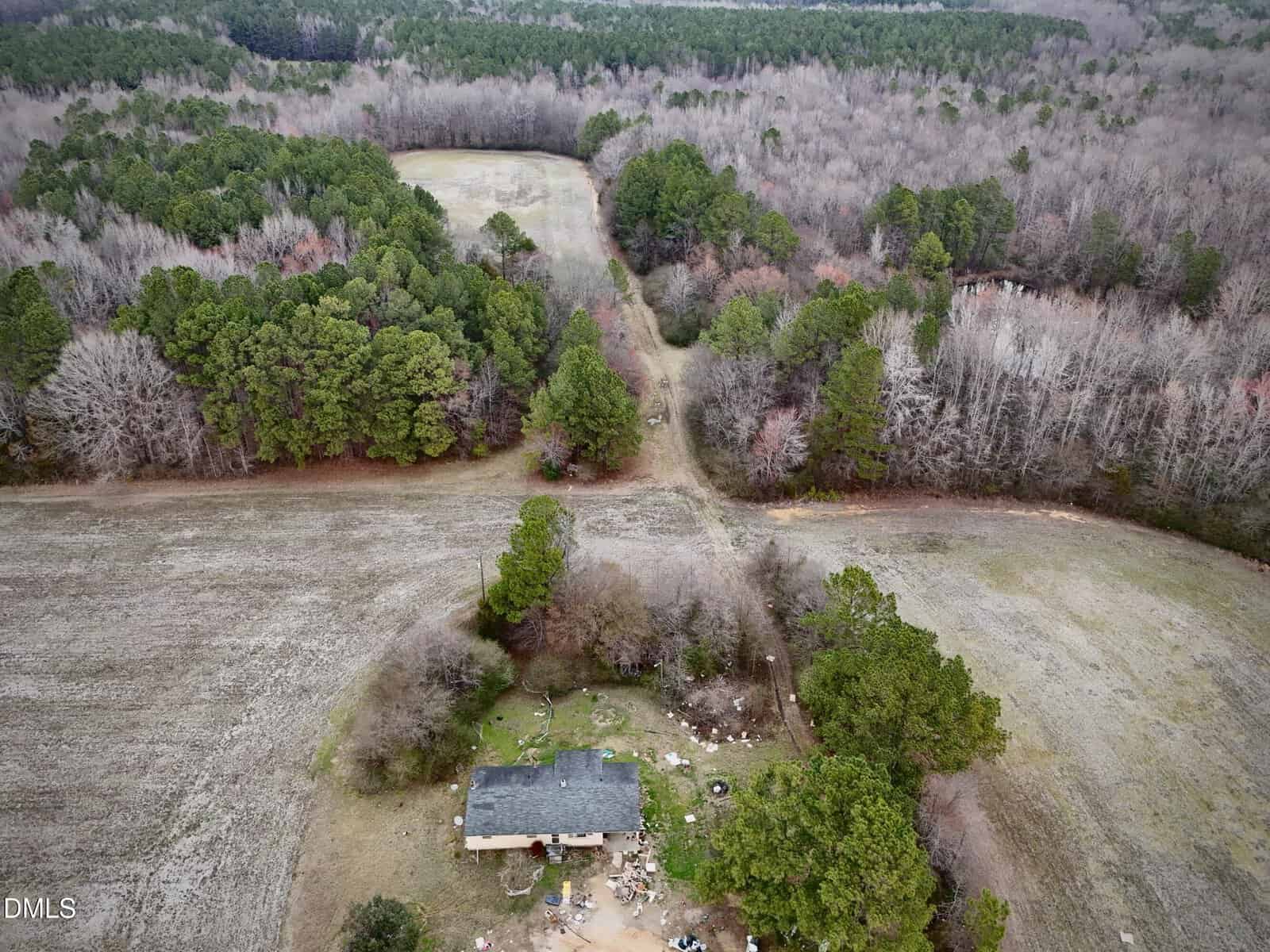 Aerial view of a house on Lot 6 W River Road in Franklinton, surrounded by wintery fields and leafless trees, with a dirt path leading into dense forest and scattered debris near the property.