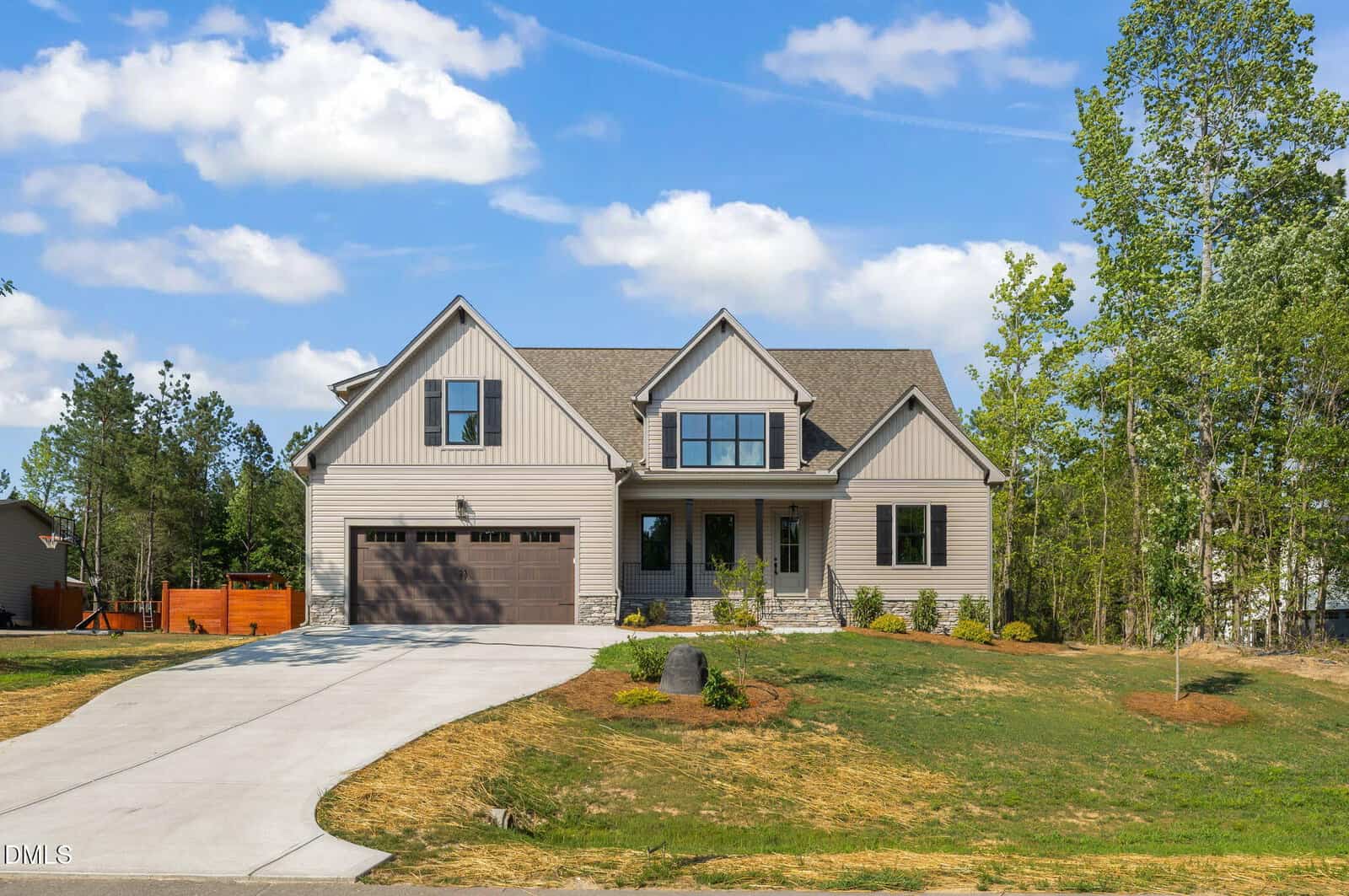 A modern two-story house with gray siding, a large garage, front porch, and landscaped yard, set on a spacious lot with trees and a clear blue sky in the background.