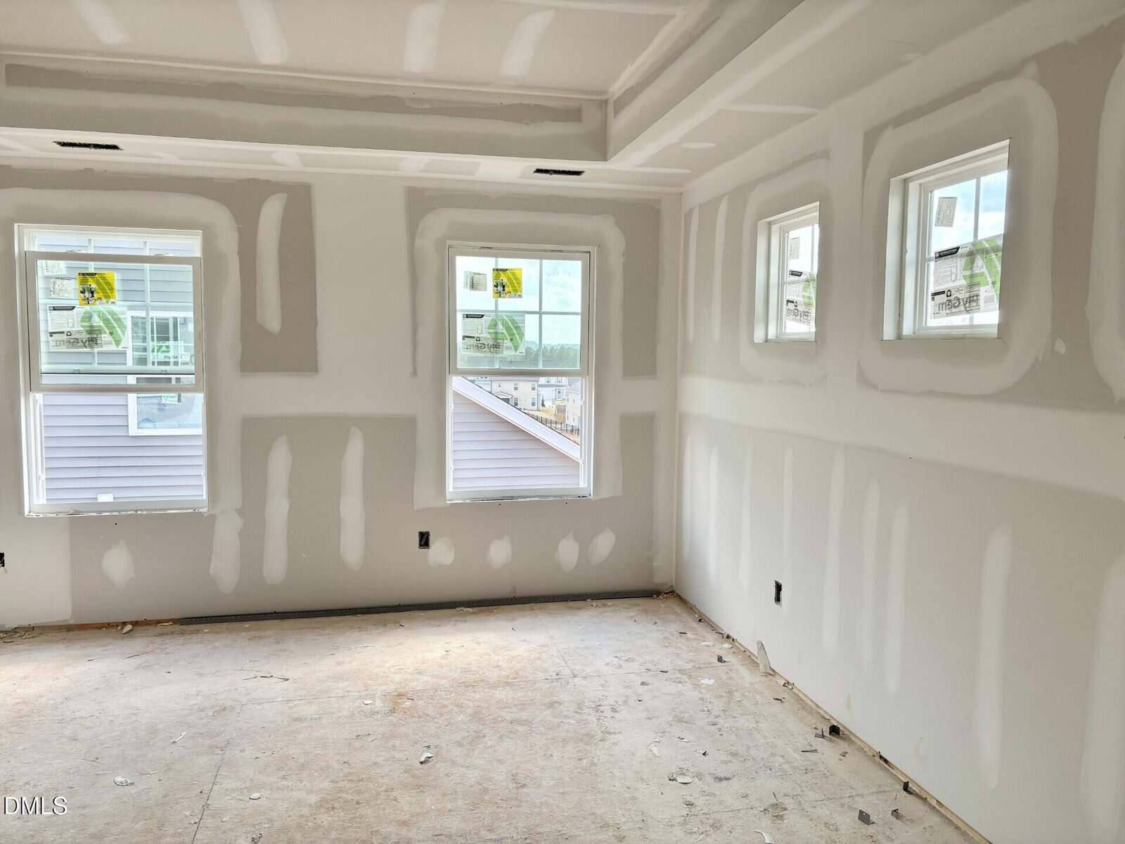 Unfinished room with drywall installed and seams taped, three windows on one wall and two on another, no flooring, and some construction debris on the floor. Natural light enters through all windows.