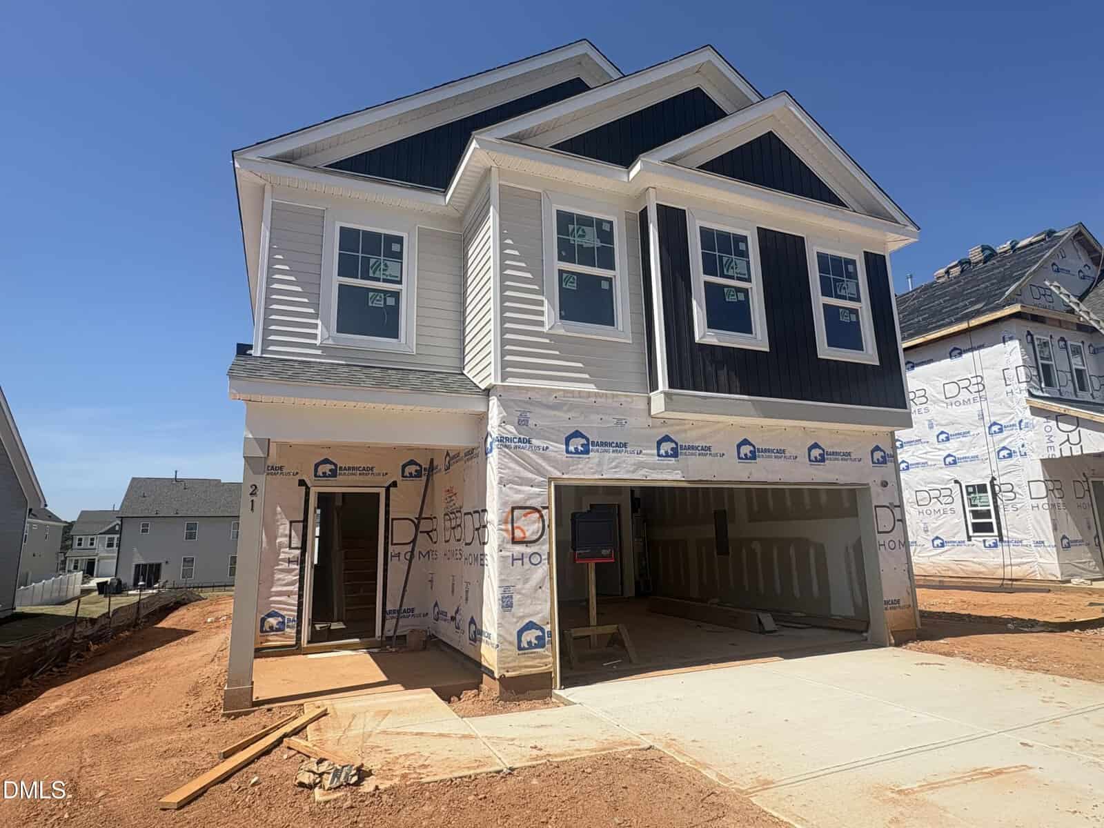 A newly constructed two-story house at 21 Gerrard Street in Franklinton features white and dark gray siding, an unfinished driveway, exposed garage interiors, and construction materials scattered on bare red soil. Other houses are visible nearby.