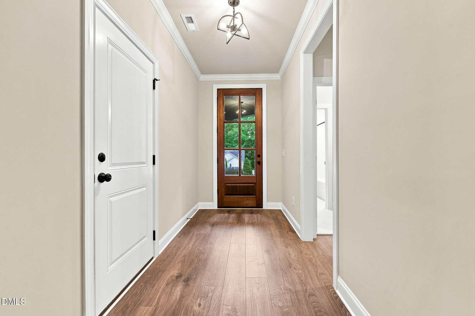 A hallway with light beige walls, wood flooring, white trim, a white door on the left, open doorways on the right, and a wooden-framed glass door at the end leading outside.