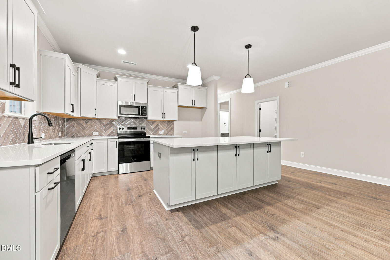 Modern kitchen with white cabinets, stainless steel appliances, large island, pendant lights, light wood floors, and a beige herringbone backsplash. Room is bright with ample counter space and an open floor plan.