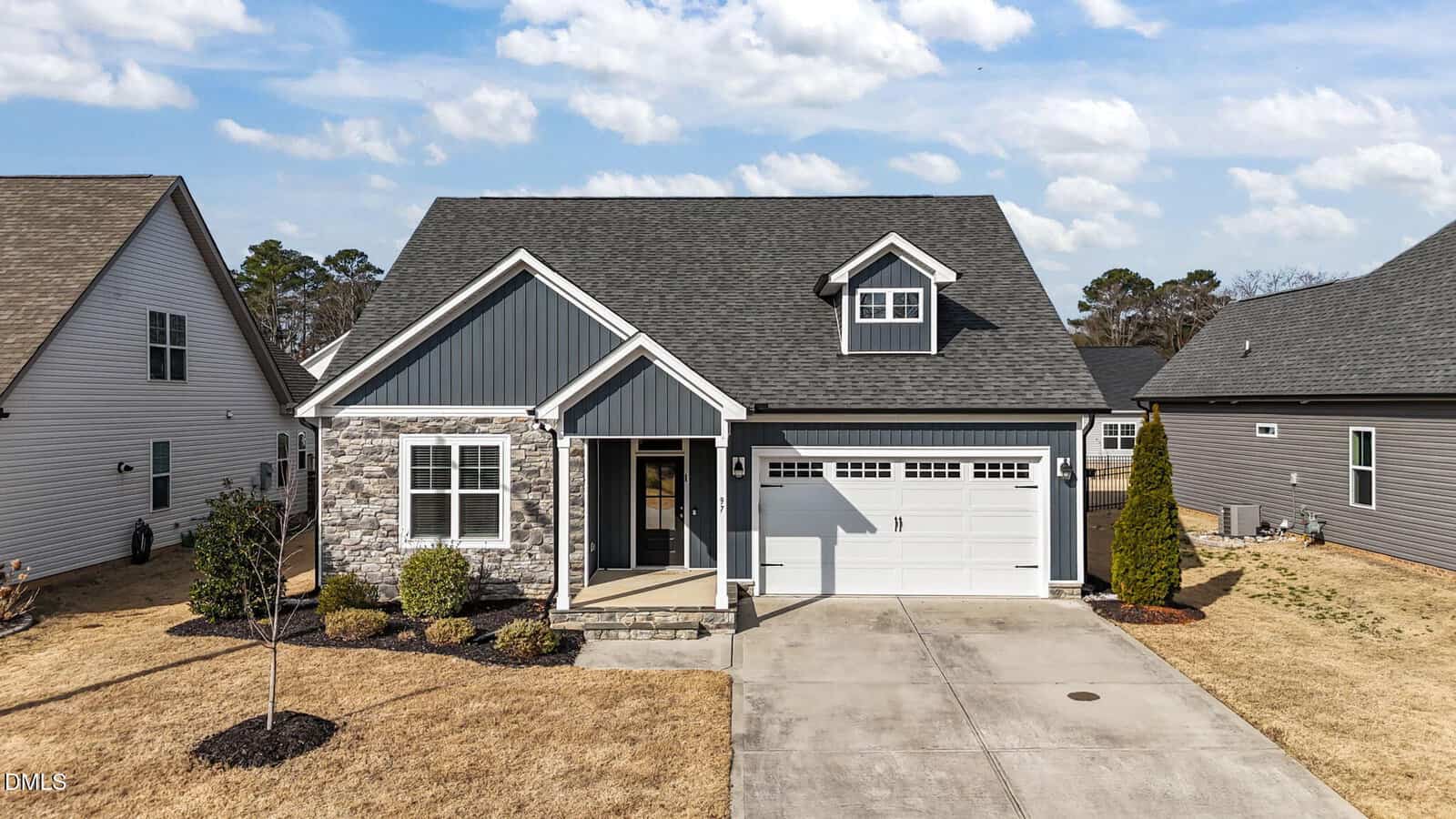 A modern single-family house with stone and siding exterior, a covered front porch, attached two-car garage, and a well-kept lawn. Located at 97 Sweetbay Park in Youngsville, the home is situated between two similar residences under a partly cloudy sky.