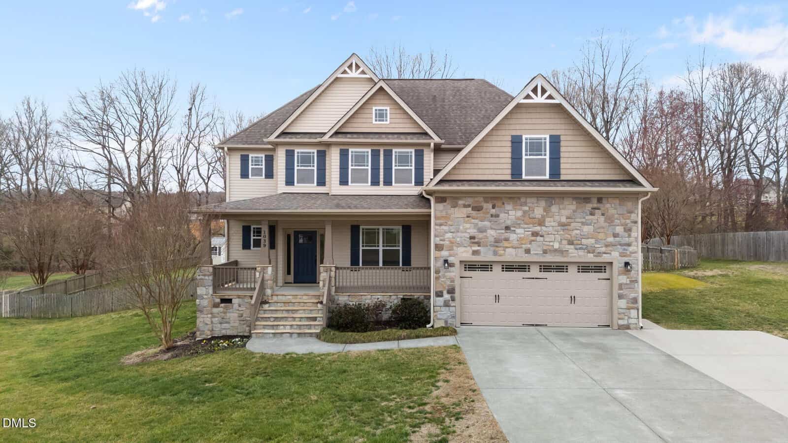 Two-story suburban house with beige siding and stone accents, covered front porch, double garage, and a spacious driveway located at 1039 Bluebell Lane in Wake Forest. The yard is partially landscaped, and leafless trees are visible in the background under a blue sky.