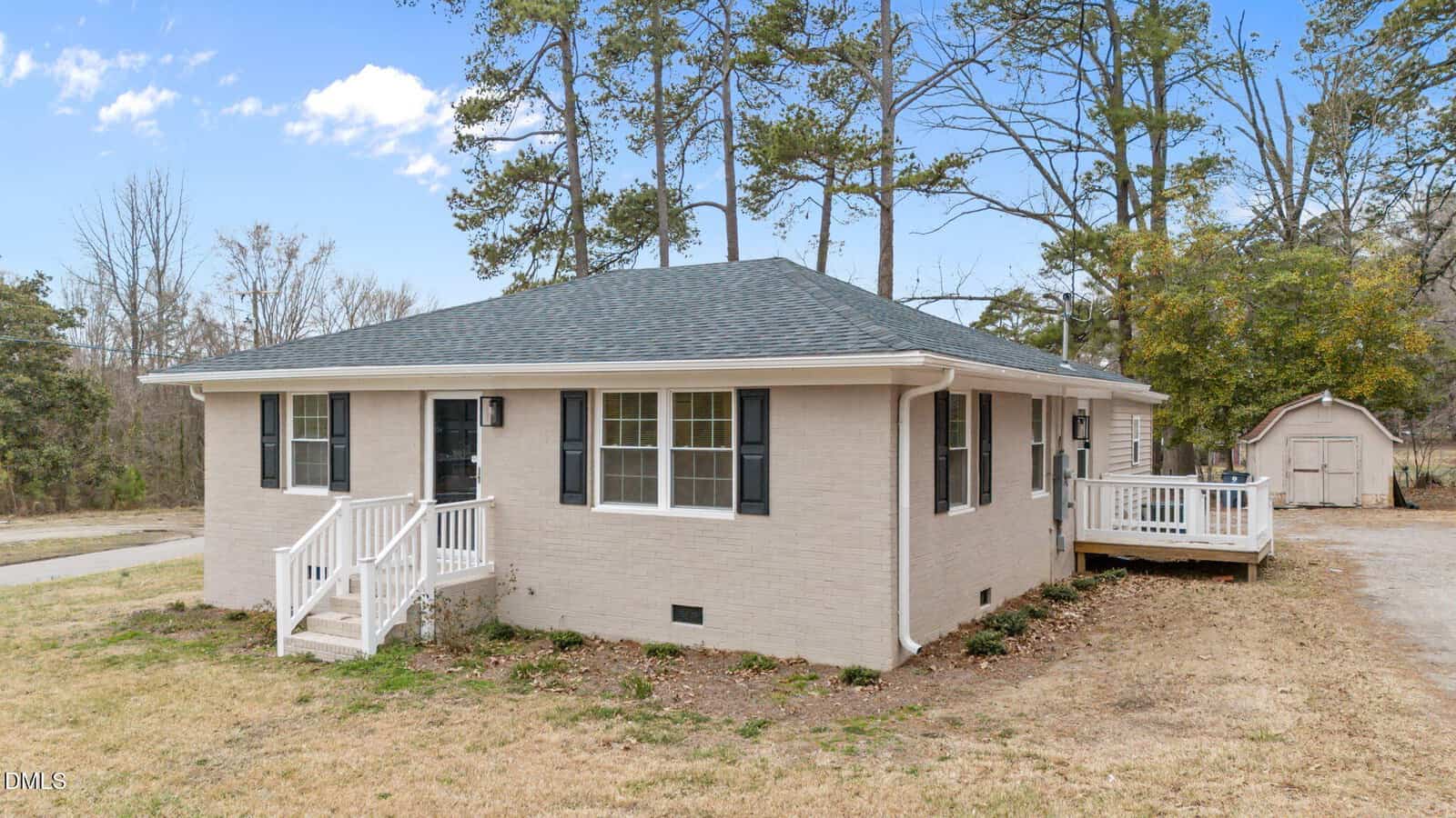 Charming single-story beige brick house with black shutters located at 118 Cherry Street, Henderson. It features a small front porch and a side deck, while the yard is mostly grass with a few shrubs. Trees and a shed are visible in the background under a partly cloudy sky.