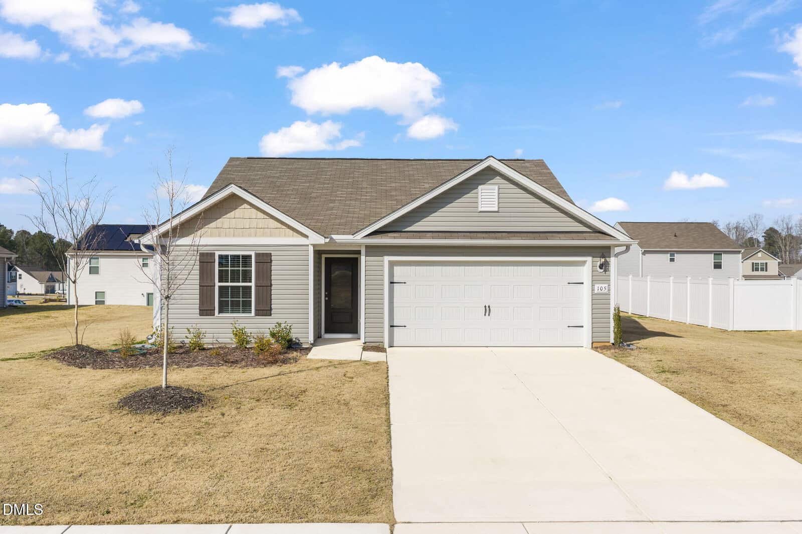 Charming one-story house at 105 Hybrid Street, Oxford, featuring gray siding, a two-car garage, and a covered front entrance. The lawn is mostly brown with minimal landscaping, while the sky remains mostly clear with just a few clouds.