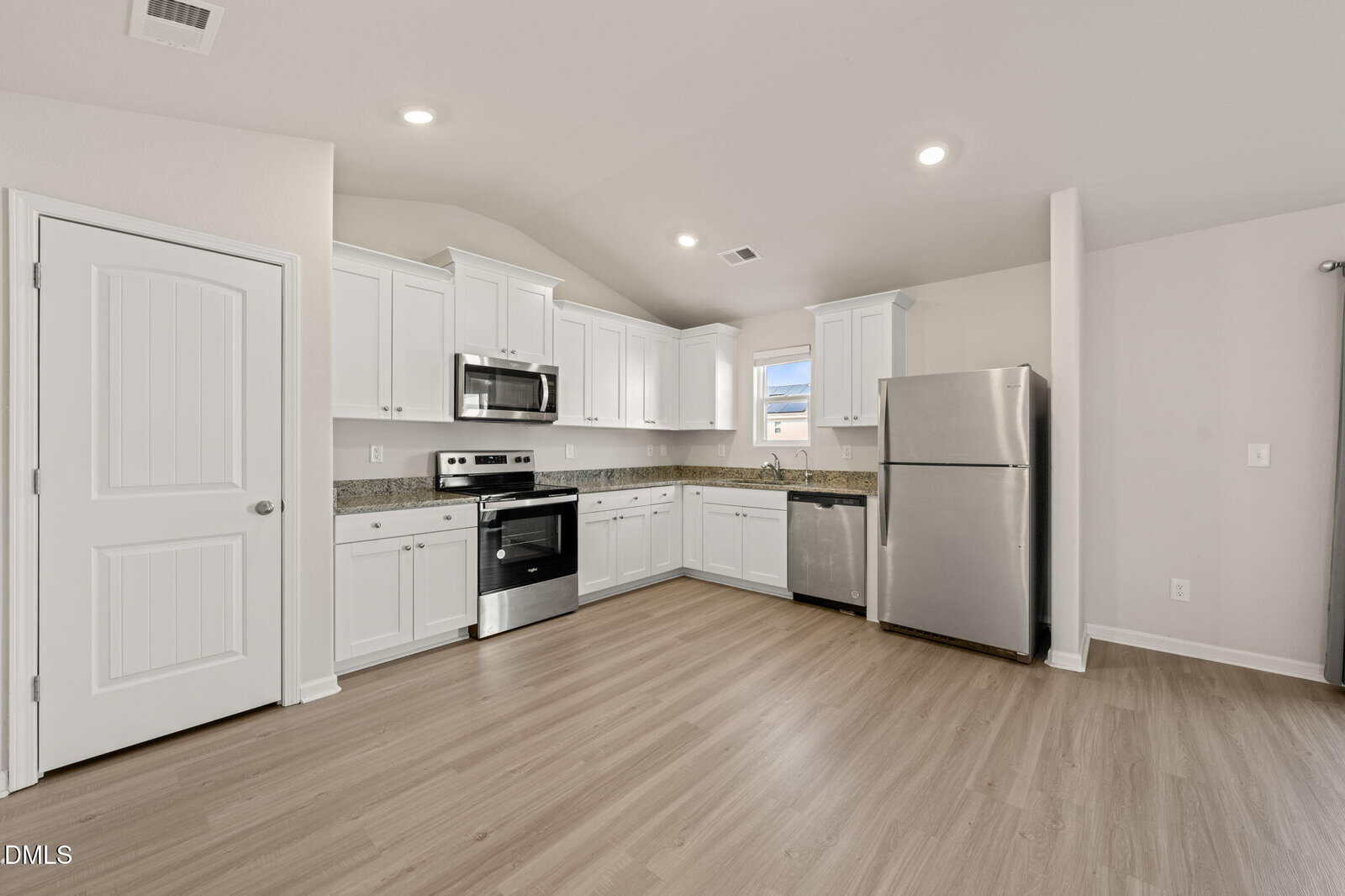 Modern kitchen with white cabinets, stainless steel appliances including a refrigerator, microwave, dishwasher, and oven, granite countertops, light wood flooring, and high ceilings under recessed lighting.