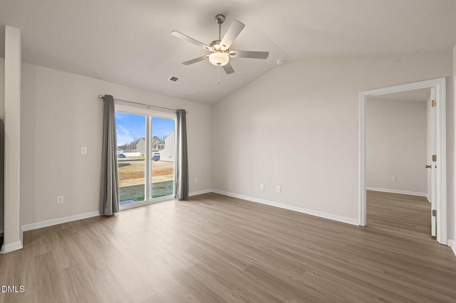 Empty room with light wood flooring, gray walls, a ceiling fan, large window with sliding glass door, and an open doorway leading to another room with similar flooring and color scheme.