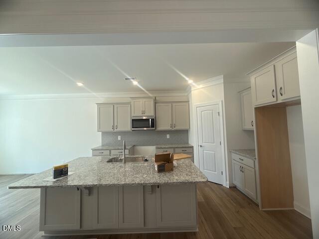 Modern kitchen with light gray cabinets, granite island countertop, stainless steel microwave, and wood flooring. There is a sink on the island, and an open cabinet section next to a closed pantry door.