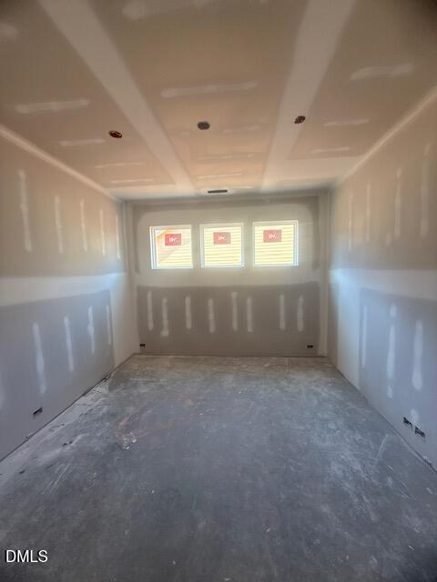Unfinished room with drywall installed on walls and ceiling, three small rectangular windows at the far end, and exposed concrete floor. Sunlight enters through the windows, and electrical outlets are visible near the base of the walls.