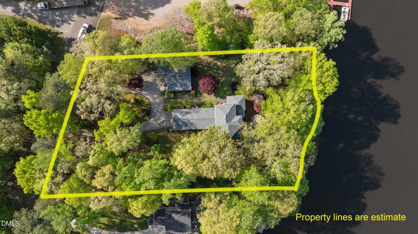 Aerial view of a house surrounded by trees near a body of water, with a yellow outline marking the estimated property lines. Text reads “Property lines are estimate.”.