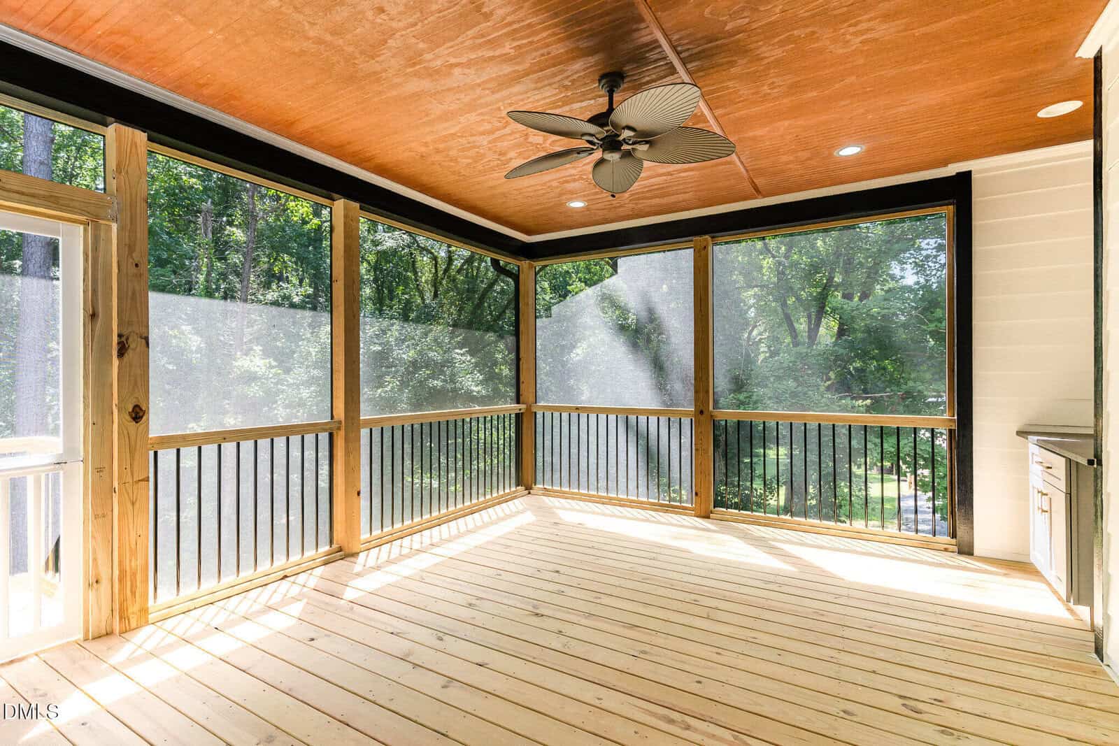 A bright, screened-in porch with wooden floors and ceiling, a ceiling fan, and views of green trees outside. Sunlight streams through the screens, creating a warm and inviting atmosphere.