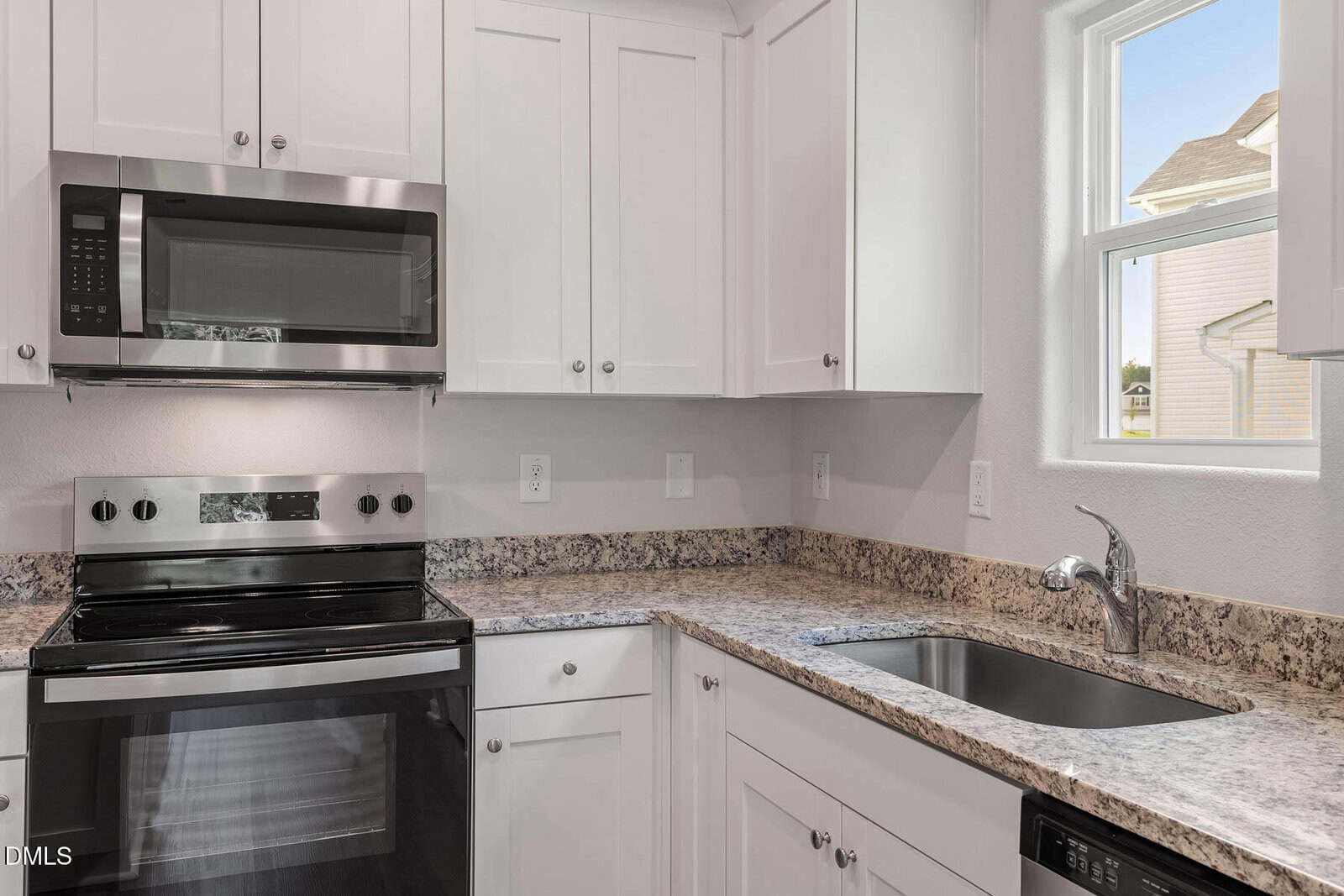 Modern kitchen with white cabinets, stainless steel oven and microwave, granite countertops, a black sink with a silver faucet, and a window letting in natural light.