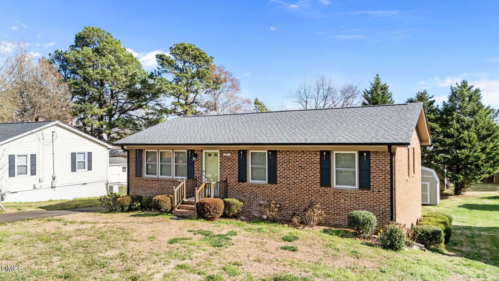 Single-story brick house with a gray shingle roof, small front porch, and minimal landscaping located at 511 Sunset Avenue in Oxford. The yard has patchy grass and is bordered by bushes. There is a white shed in the backyard, and trees in the background.