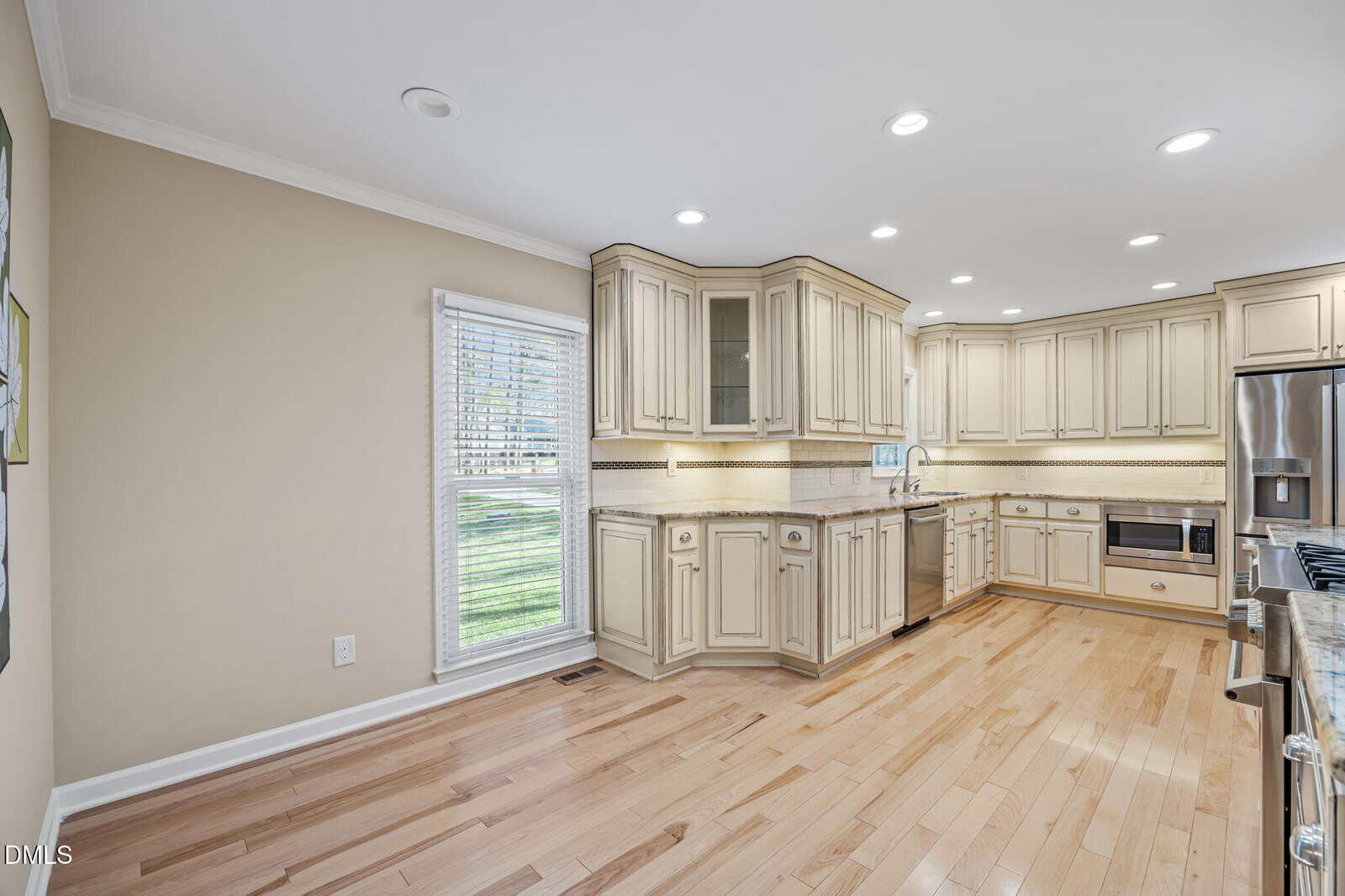Spacious kitchen with light wood floors, cream-colored cabinets, stainless steel appliances, and a large window letting in natural light.
