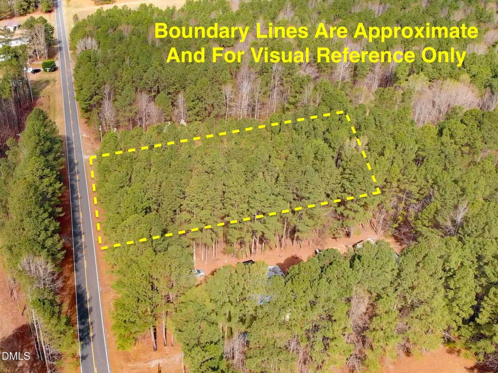 Aerial view of a wooded lot outlined with yellow dashed lines near a road; text reads “Boundary Lines Are Approximate And For Visual Reference Only.”.