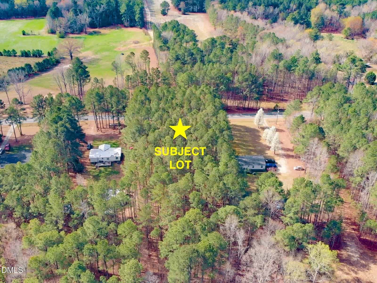 Aerial view of a wooded area with two houses, a road, and a yellow star labeled “SUBJECT LOT” marking a specific plot among the trees.