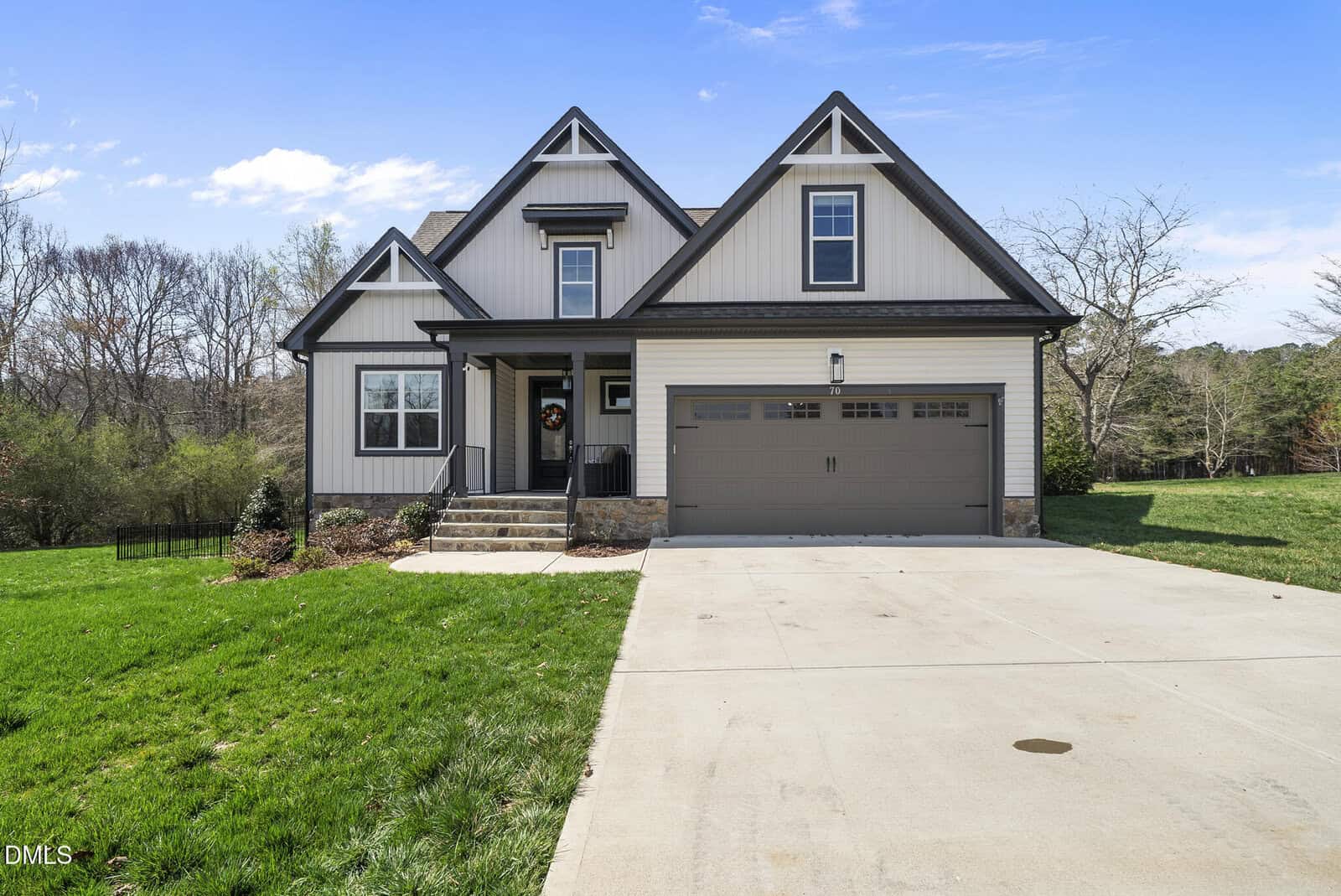 A modern two-story house with gray siding, black trim, a covered front porch, and a double garage sits on a concrete driveway. The lawn is green and well-maintained, with trees in the background.