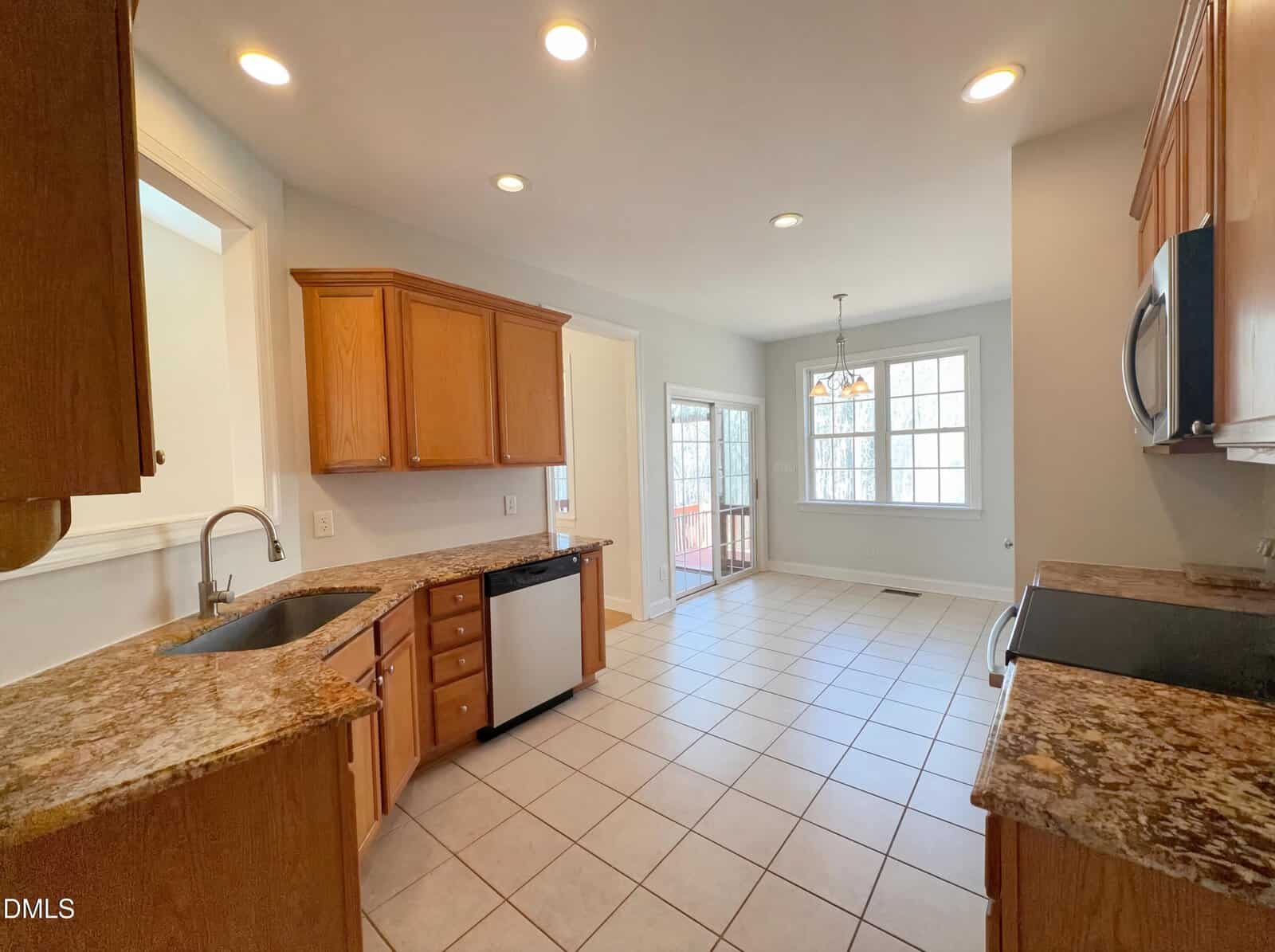 Spacious kitchen with wood cabinets, granite countertops, stainless steel appliances, tiled floor, and a dining area with large windows letting in natural light.