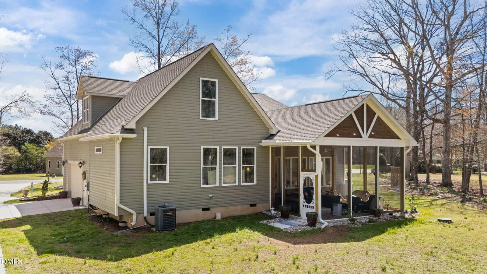 Light brown single-story house with gable roof, white trim, and a screened porch. Several windows line the side. The yard is mostly grass with some bare patches, and trees without leaves are visible in the background.